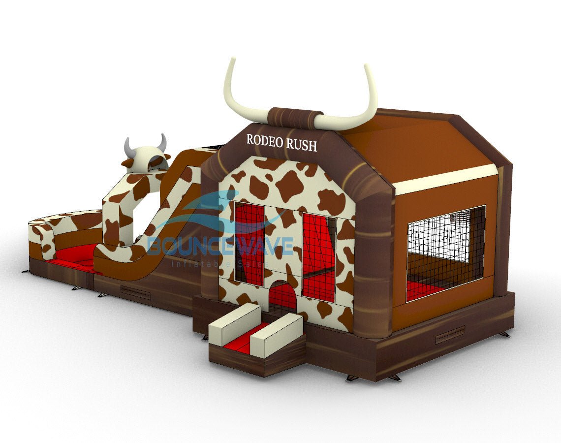 Front view of Rodeo Rush Dual Lane Commercial Inflatable Combo set up in a large indoor warehouse. The inflatable features a brown base with cow print patterns, a bull-shaped figure with slides, and a bounce house area. Large white horns top the structure, and "RODEO RUSH" is visible. Metal roofing and various other inflatable products are visible in the background.