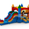 Three-quarter view of Seasonal Sampler Commercial Econo Inflatable Panel Combo displaying a Halloween scene on the panel. The inflatable includes colorful castle-like towers, dual slides in red and blue, and a bounce house area. The structure is set on a blue base with yellow entrance steps and features multiple spires in various colors.
