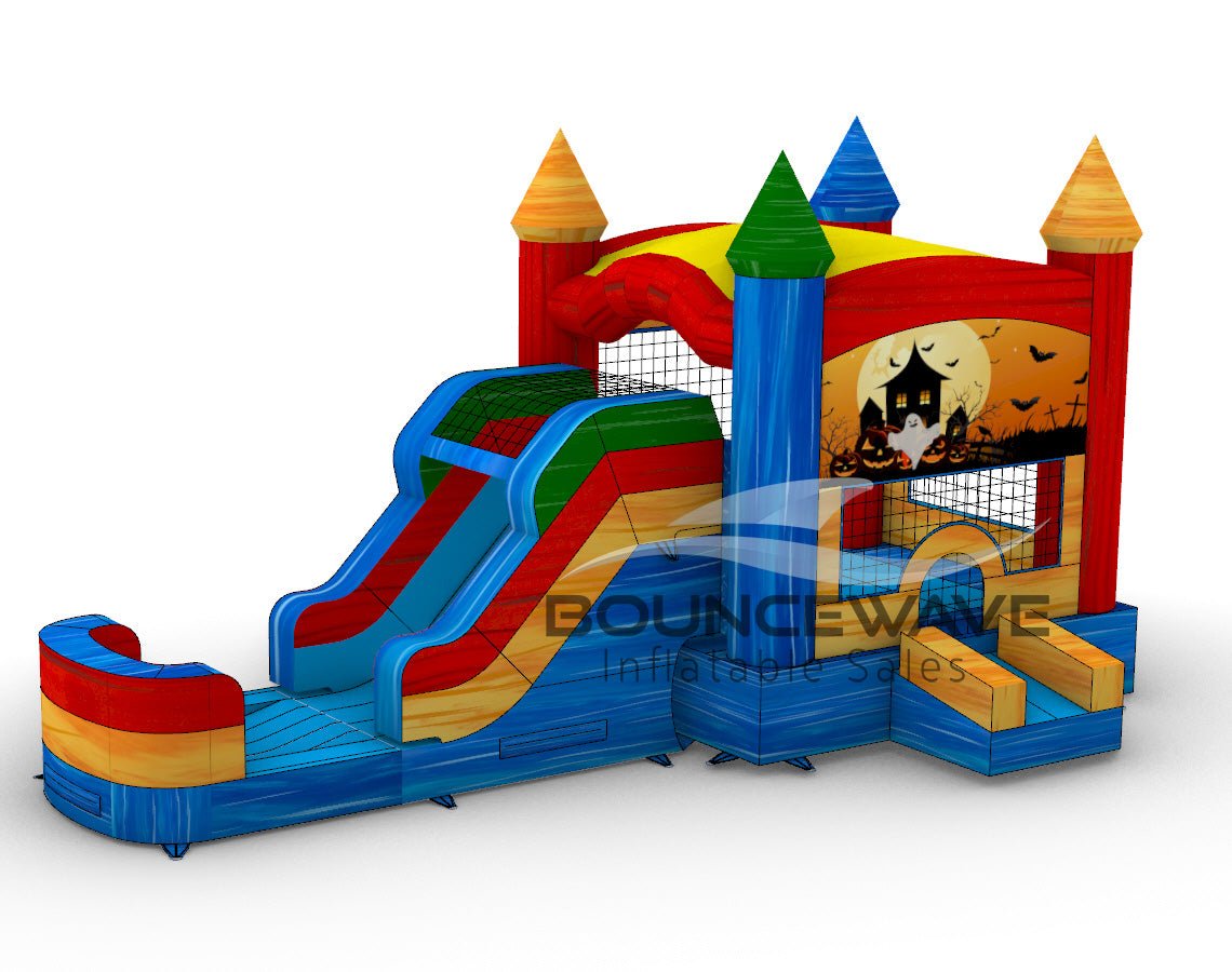 Three-quarter view of Seasonal Sampler Commercial Econo Inflatable Panel Combo displaying a Halloween scene on the panel. The inflatable includes colorful castle-like towers, dual slides in red and blue, and a bounce house area. The structure is set on a blue base with yellow entrance steps and features multiple spires in various colors.
