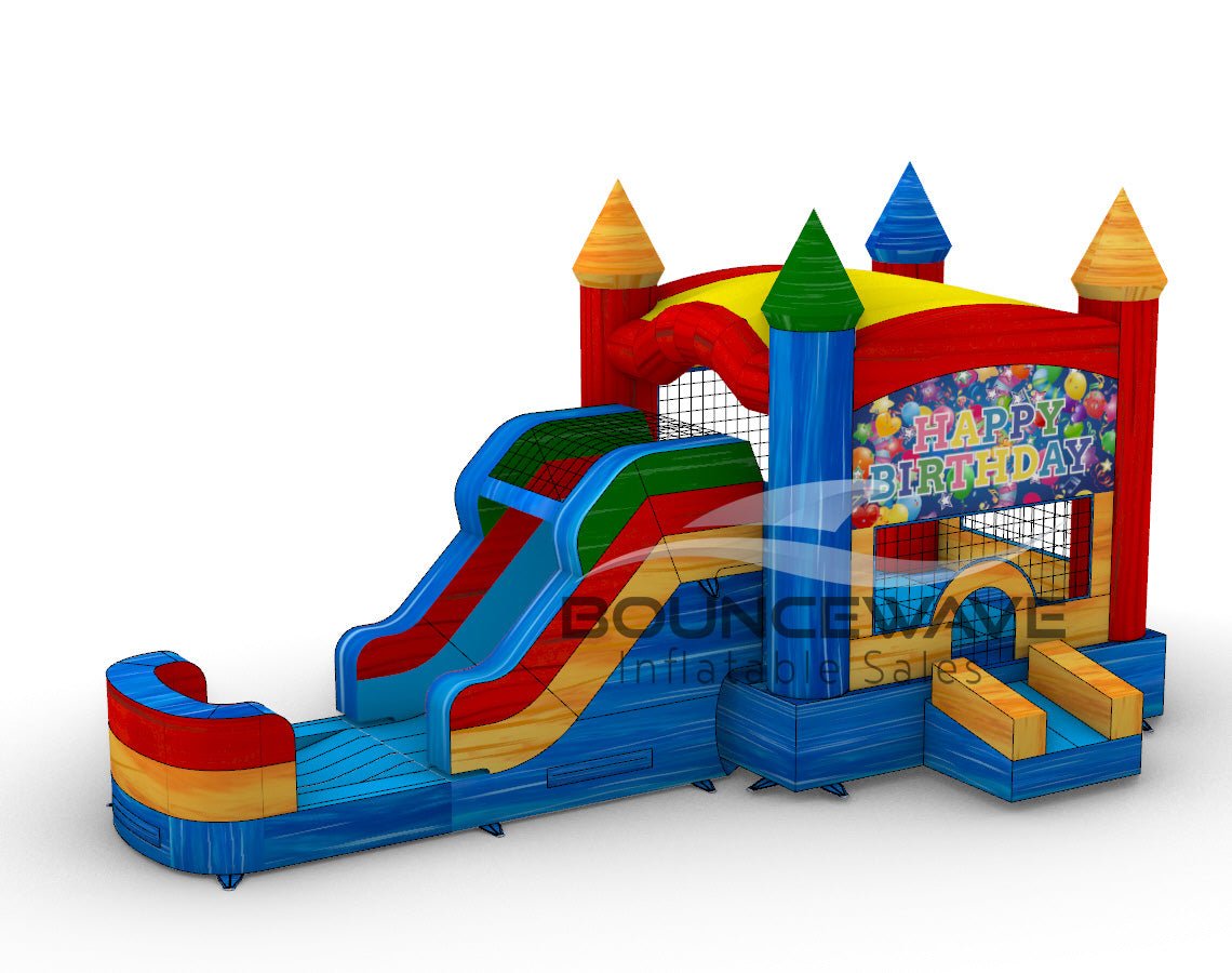 Front view of Seasonal Sampler Commercial Econo Inflatable Panel Combo featuring a "Happy Birthday" themed panel with colorful balloons and festive text. The inflatable structure has castle-like towers in red, blue, and yellow, dual slides in red and blue, and a bounce house area with mesh windows. Set on a blue base with yellow entrance steps.
