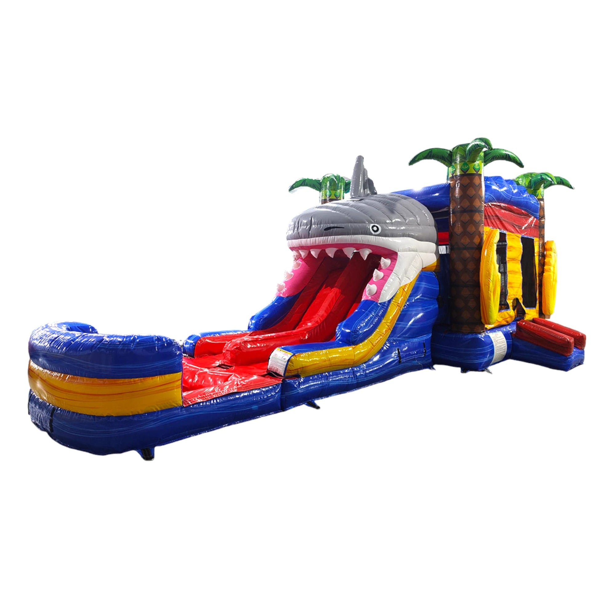 Side view of Shark Attack Dual Lane Commercial Inflatable Combo featuring a large gray shark head with open mouth and teeth. The structure includes dual slides emerging from the shark's mouth, one red and one yellow, leading to a blue splash pool. Inflatable palm trees flank the sides. Set against a white background, showcasing its ocean-themed design for commercial wet/dry use.