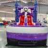 Wide-angle view of Spooky Splash Halloween Dual Lane Commercial Inflatable Combo (Wet/Dry) set up in a large indoor warehouse. The inflatable features blue castle towers, dual slides in red and purple, and a large orange jack-o'-lantern on top. A white inflatable ghost figure is perched between the slides. The front panel displays a colorful Halloween scene with pumpkins, ghosts, and other spooky elements. A white and purple splash pool area is visible at the base. The warehouse setting shows metal roofing,