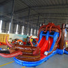 Front view of Tentacle Typhoon Dual Lane Commercial Inflatable Combo featuring a pirate ship theme with large octopus tentacles. The structure has dual slides, one red and one blue, emerging from a brown ship-like base. Inflatable octopus tentacles in red surround the sides. Pirate flags with skull and crossbones adorn the top. Set up in a large indoor warehouse with metal roofing and bright lighting visible.