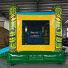 Rear view of Tiki Wave Commercial Econo Inflatable Combo (Wet/Dry) featuring a vibrant yellow bounce house with green tiki face pillars, blue top, and mesh entrance. Includes a curved blue slide, inflatable steps, and a green base. Set up in an indoor warehouse with other inflatables visible in the background.